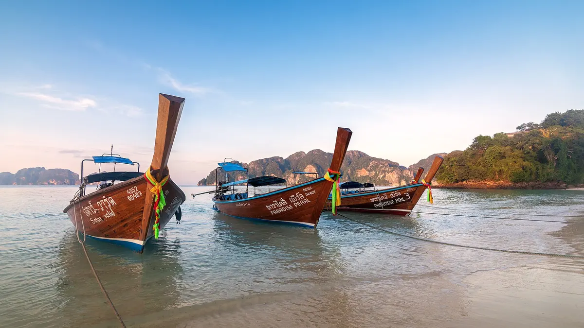 Longtail boats moored on the beach at Koh Phi Phi Don, with limestone cliffs behind